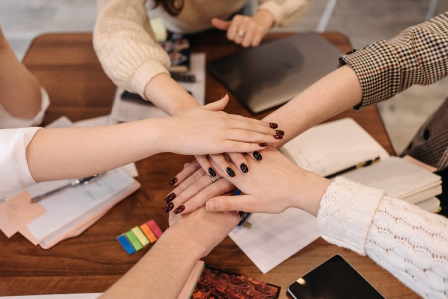 Hands stacked in teamwork gesture over a table with office items symbolizing collaboration.
