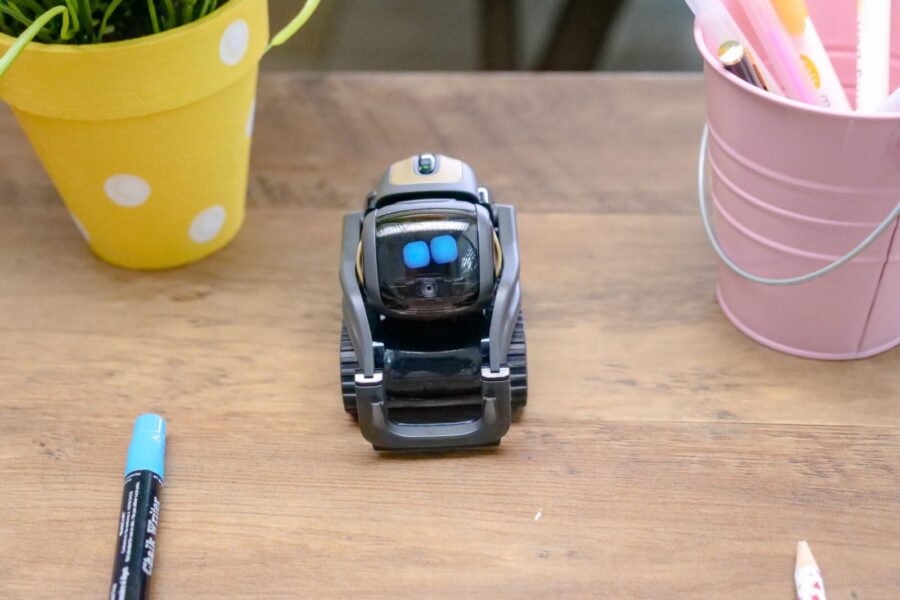 A small modern robot placed on a wooden desk surrounded by office supplies, showcases innovative technology.